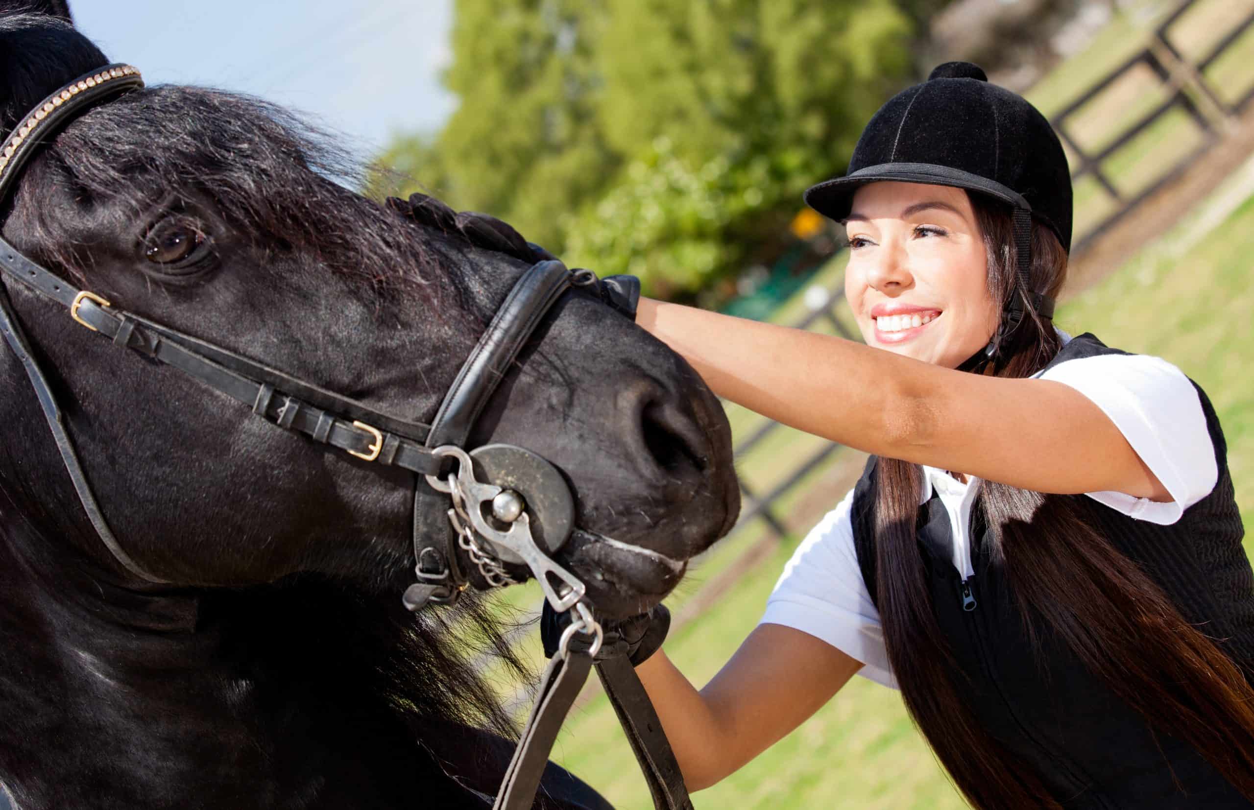 Portrait of a happy female jockey stroking a horse horseback tips
