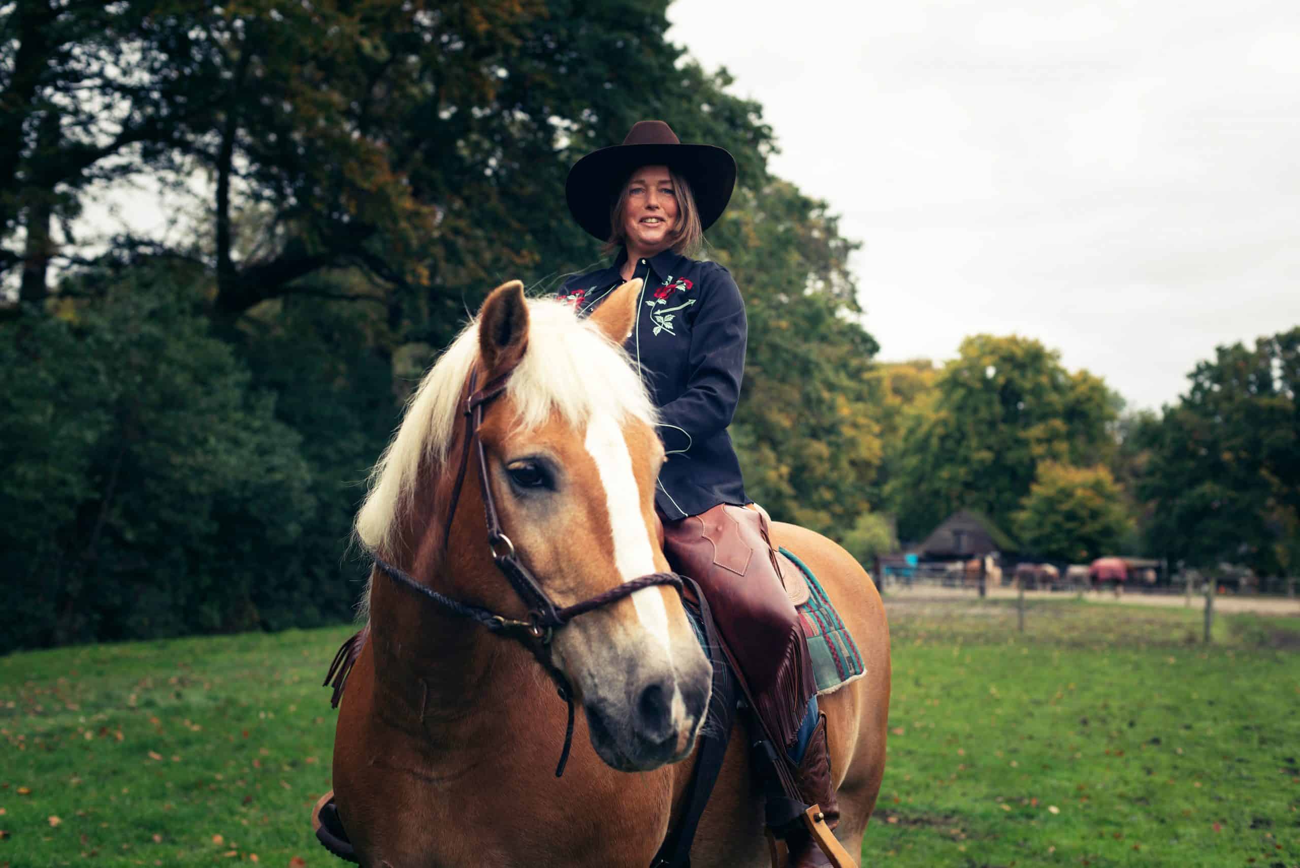 Smiling western style woman horse riding in countryside.