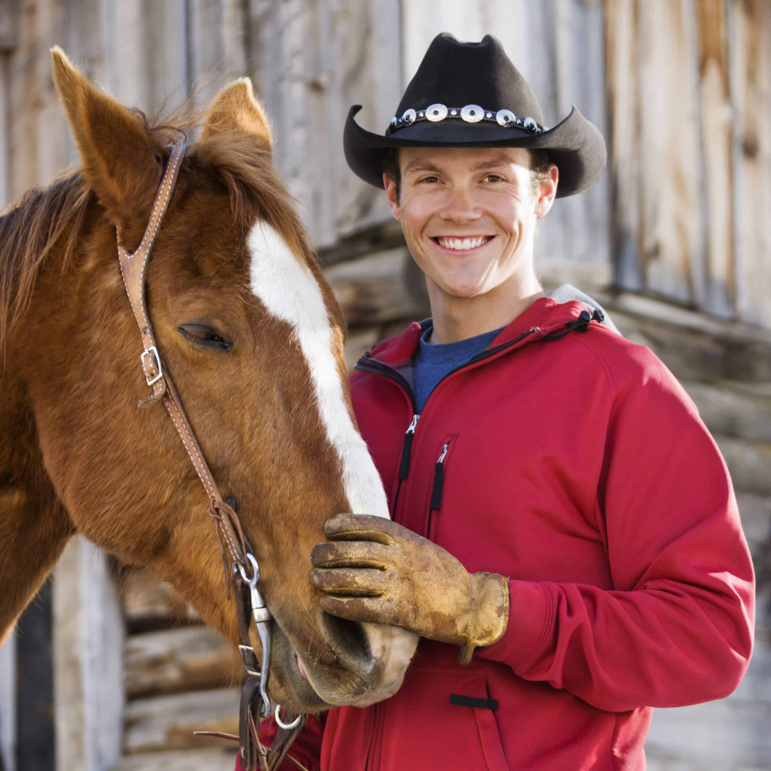 Young man in cowboy hat petting his horse.