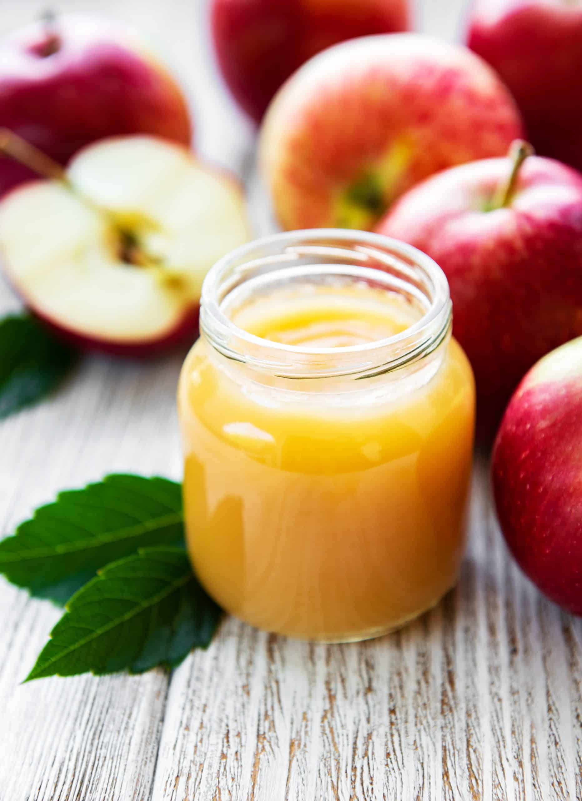 Applesauce in glass jar and fresh apples on a wooden table