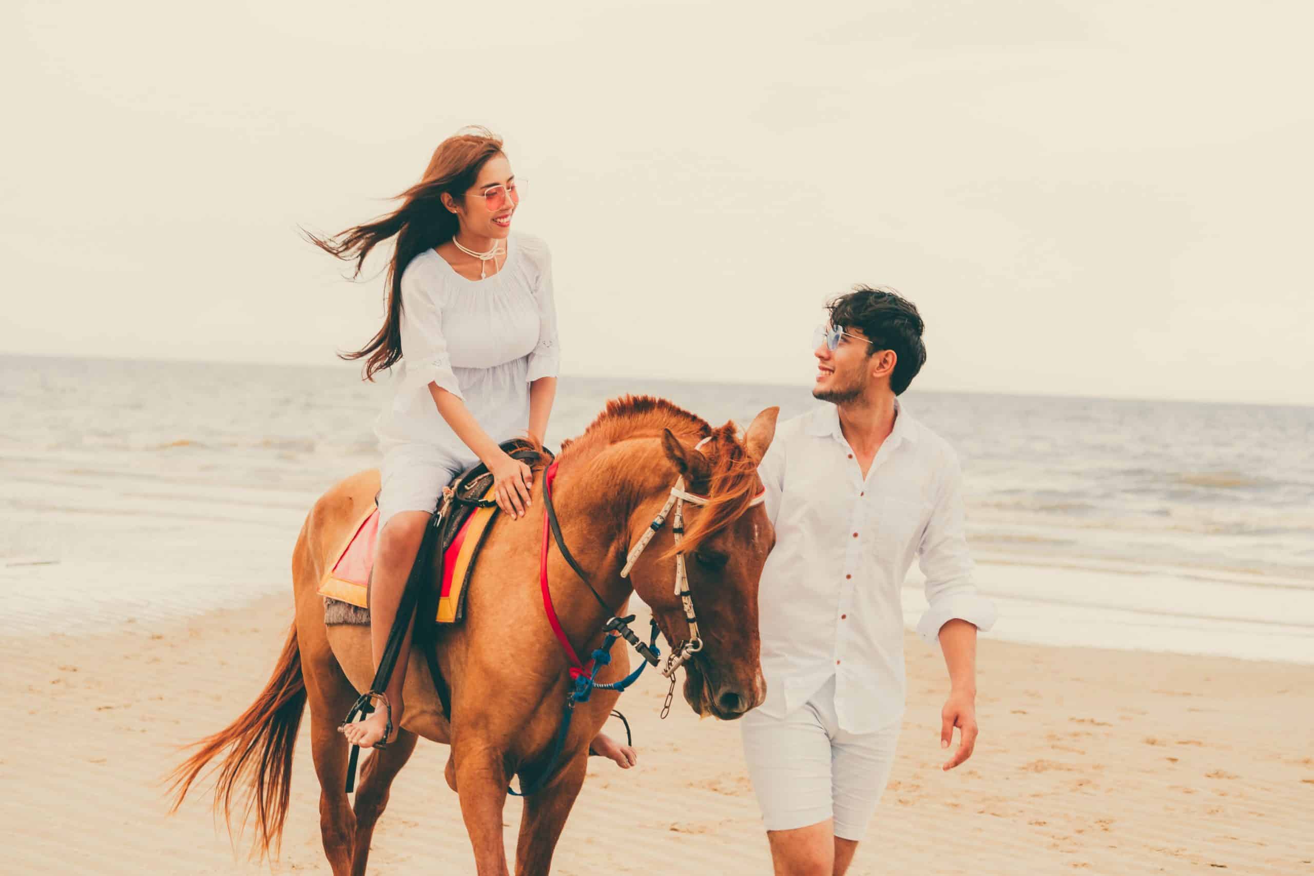 Young couple goes honeymoon horse riding on the beach in summer vacation.