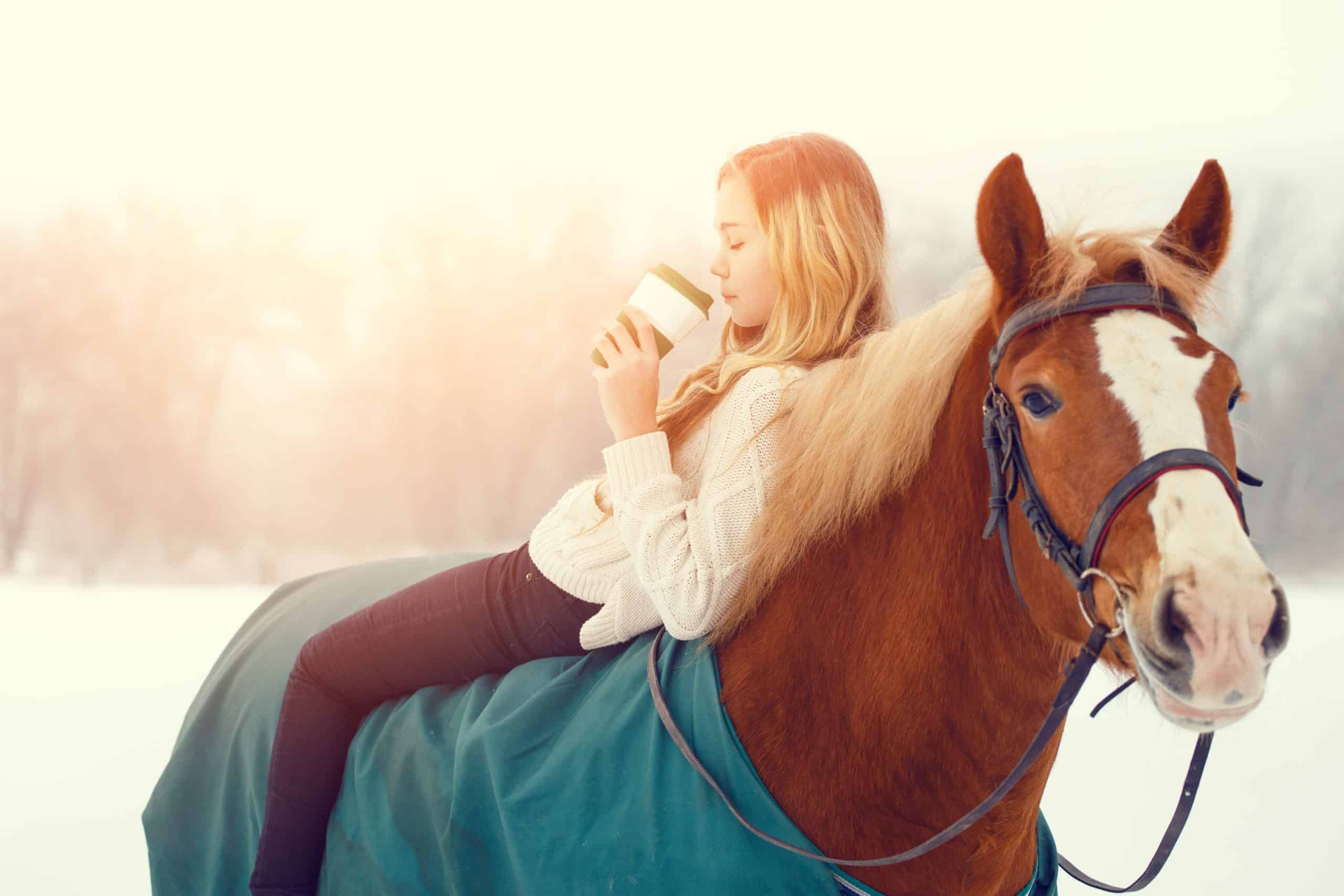 Young rider girl relaxing on horseback with cup of coffee in sunset beams