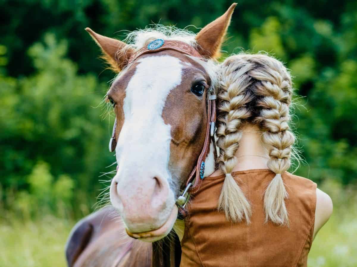Blonde in braids hugging horse