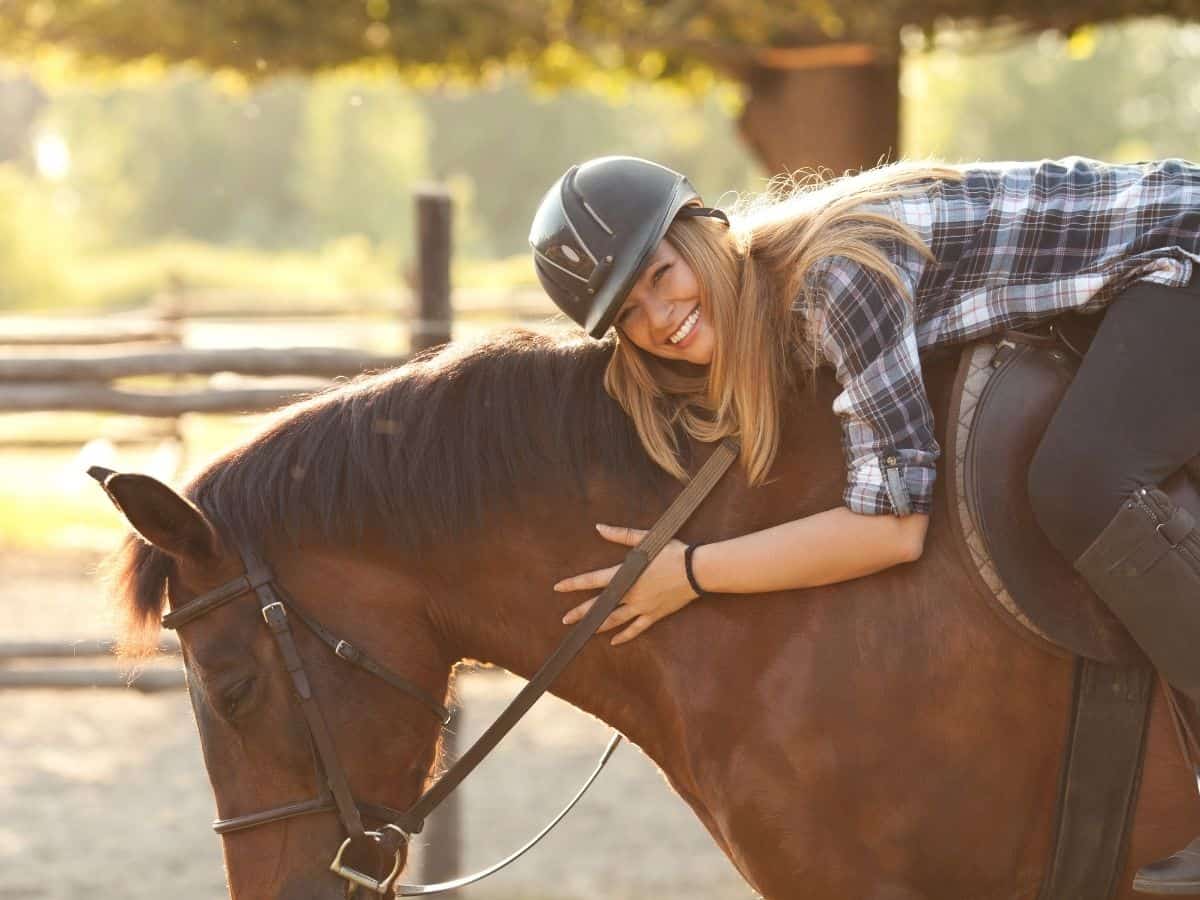 Girl with riding hat laying on horse to hug
