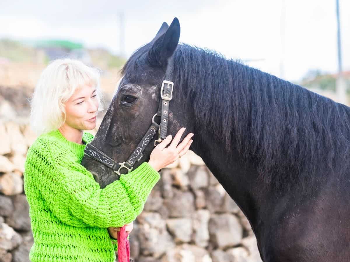 Woman in green holding black horse reigns