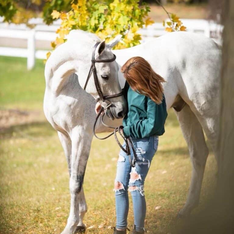 A young woman pets a white horse.