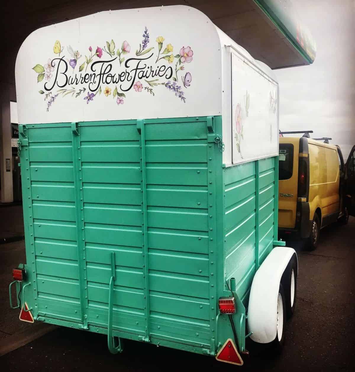 A green horse trailer painted with flower illustrations.