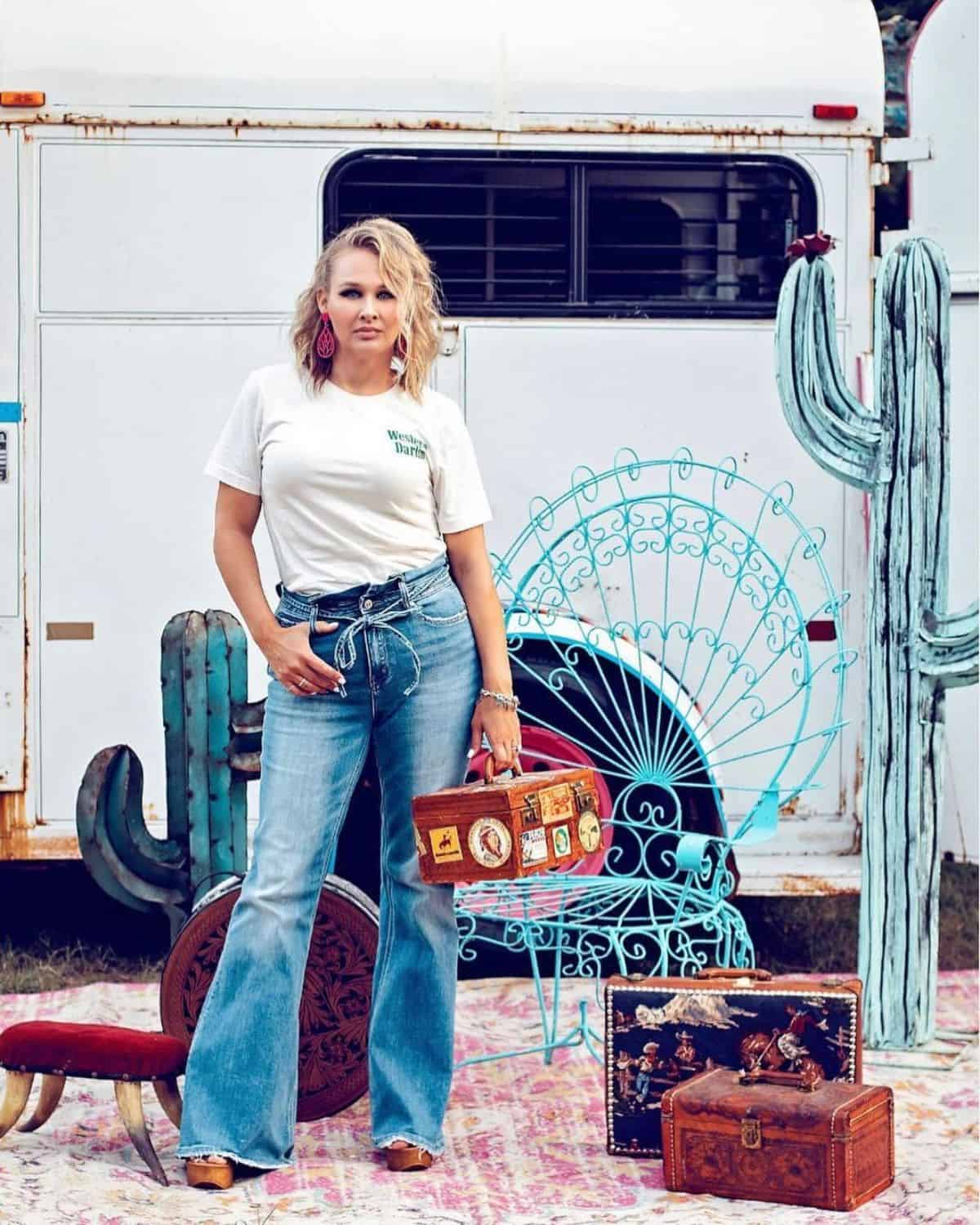 A woman stands infront of a white horse trailer.