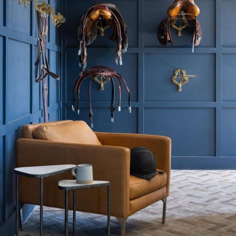 An elegant-looking tack room with horse accessories hanging on a wall and a leather armchair.