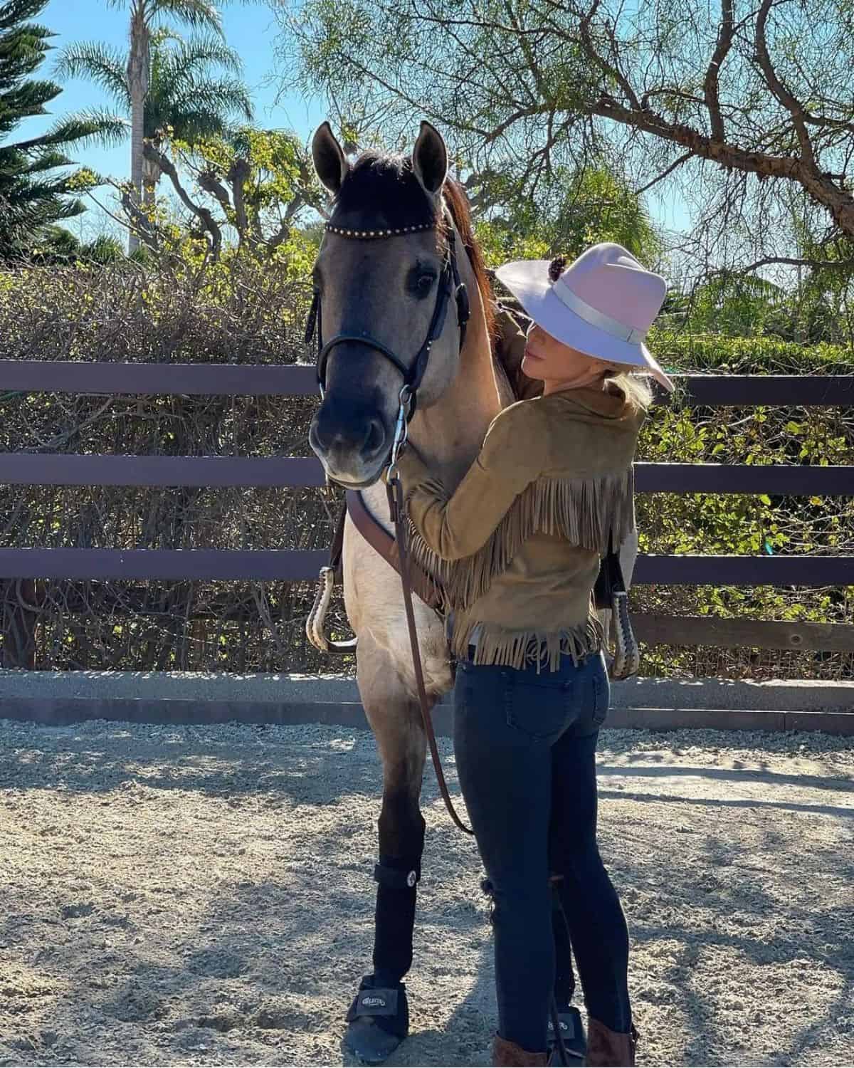 Lady Gaga stands near a brown horse.