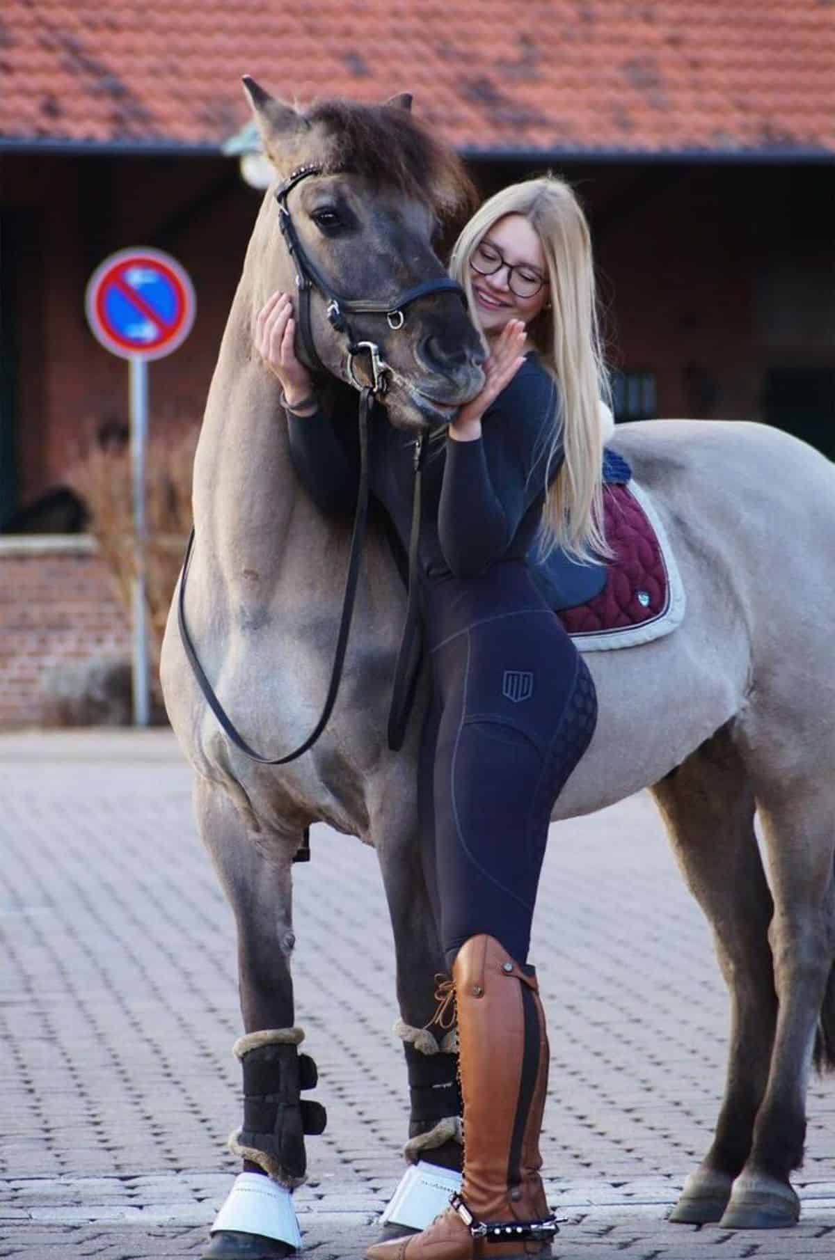 A young woman pets a gray horse.