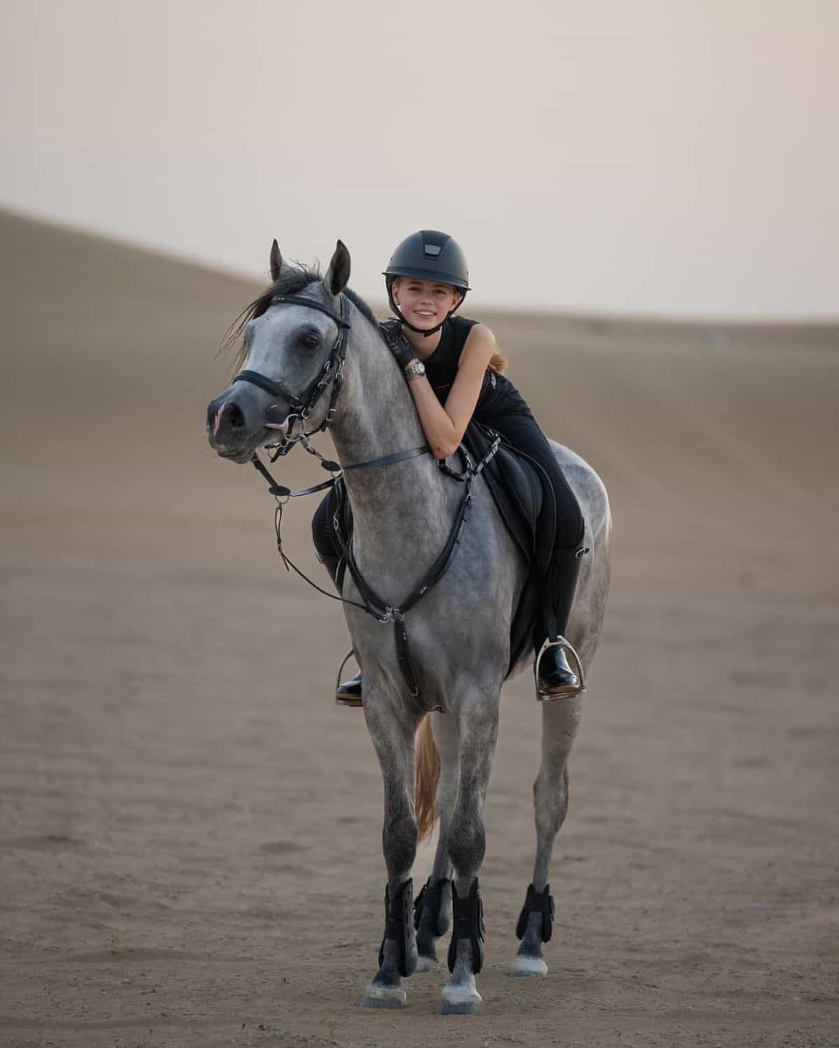 A young girl sits on a gray Arabian horse.