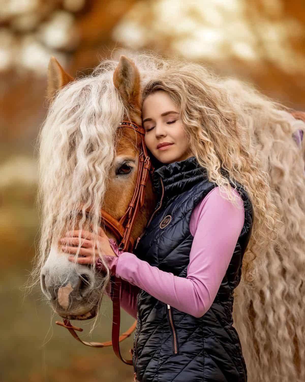 A young woman pets a brown horse with a curly mane.