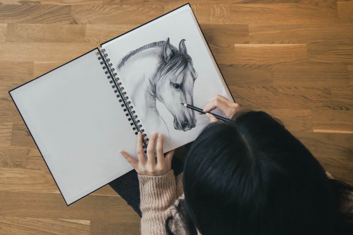 A young woman drawing a horse in a notebook.