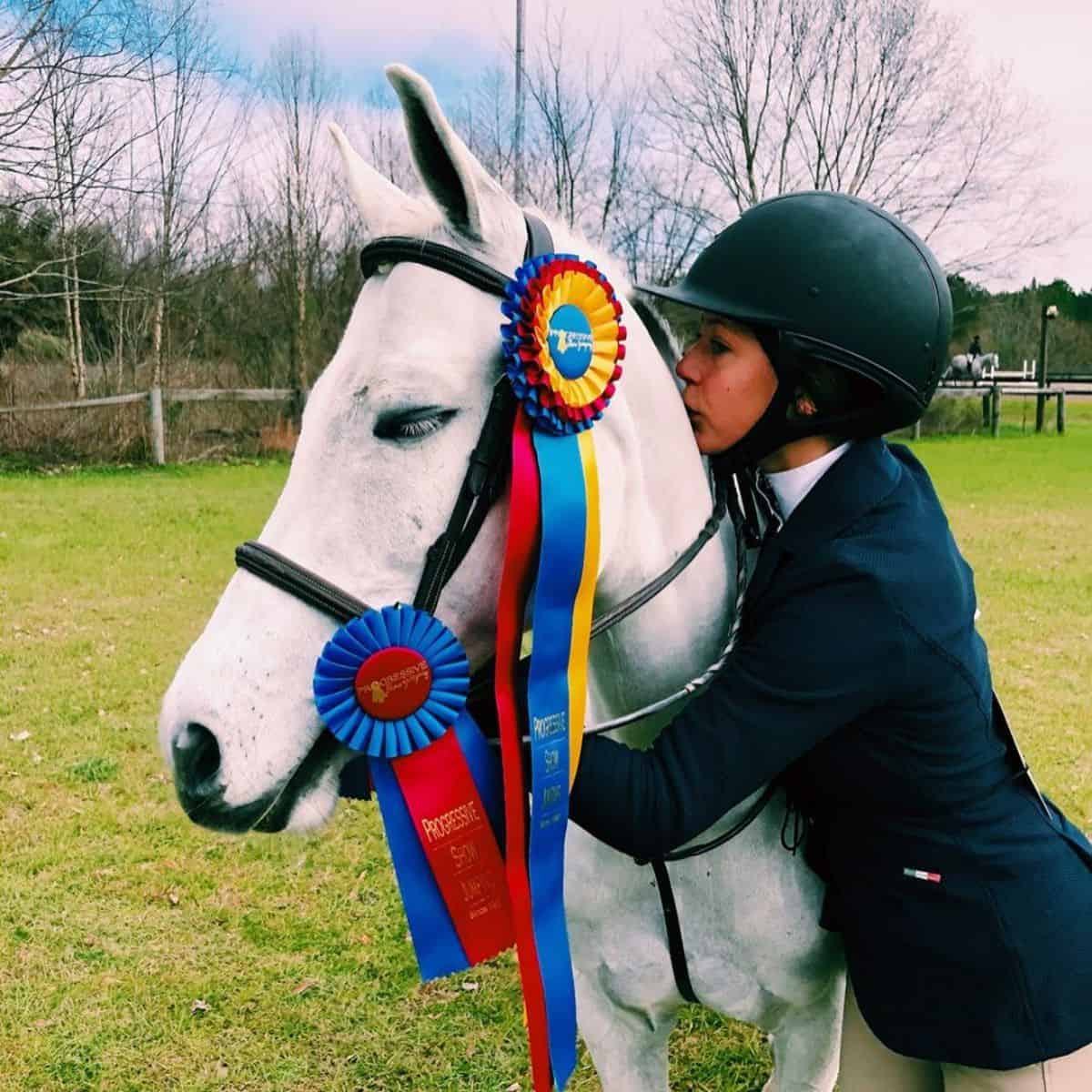 A horse rider hugging and kissing a white horse.