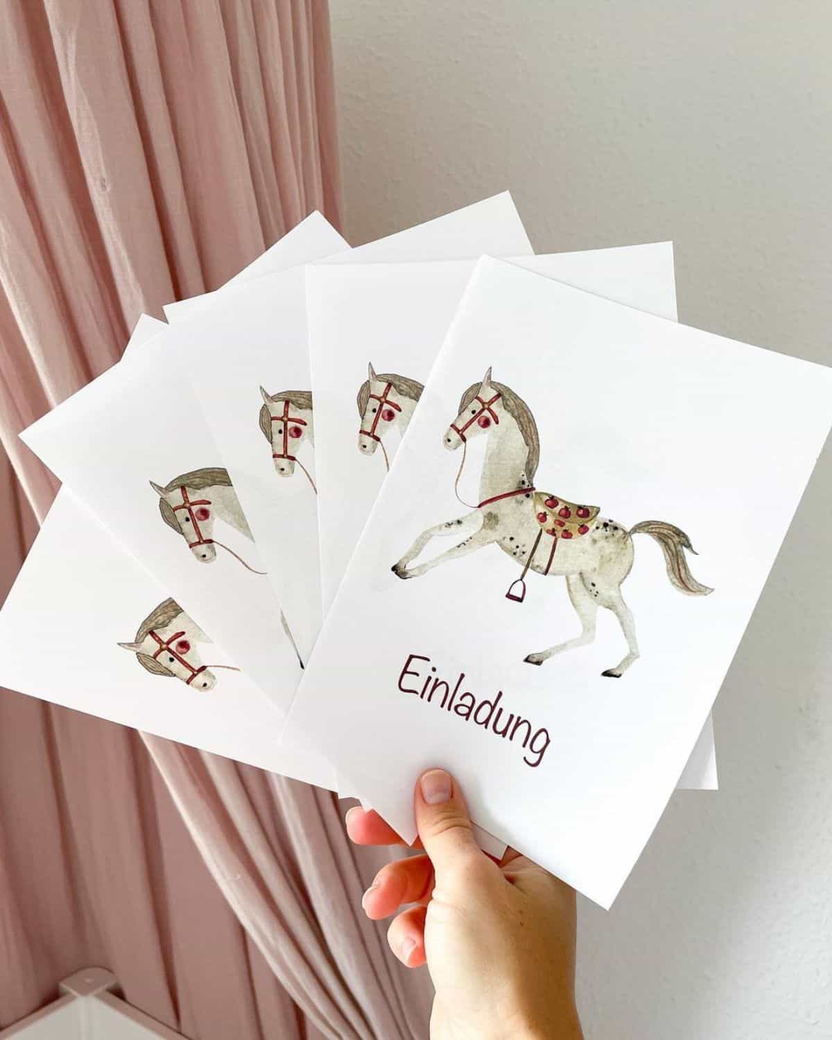 A hand holding horse-inspired party invitations.