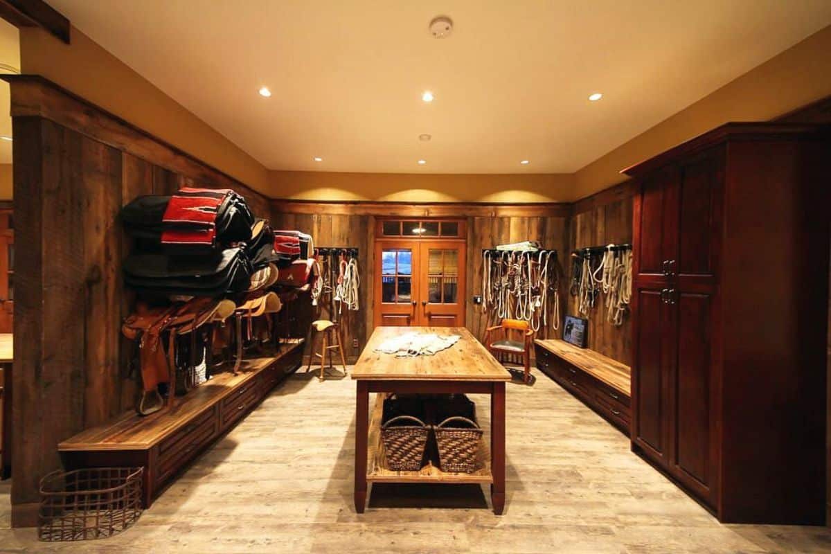 A tack room filled with saddled and other horse accessories with a big wooden table.