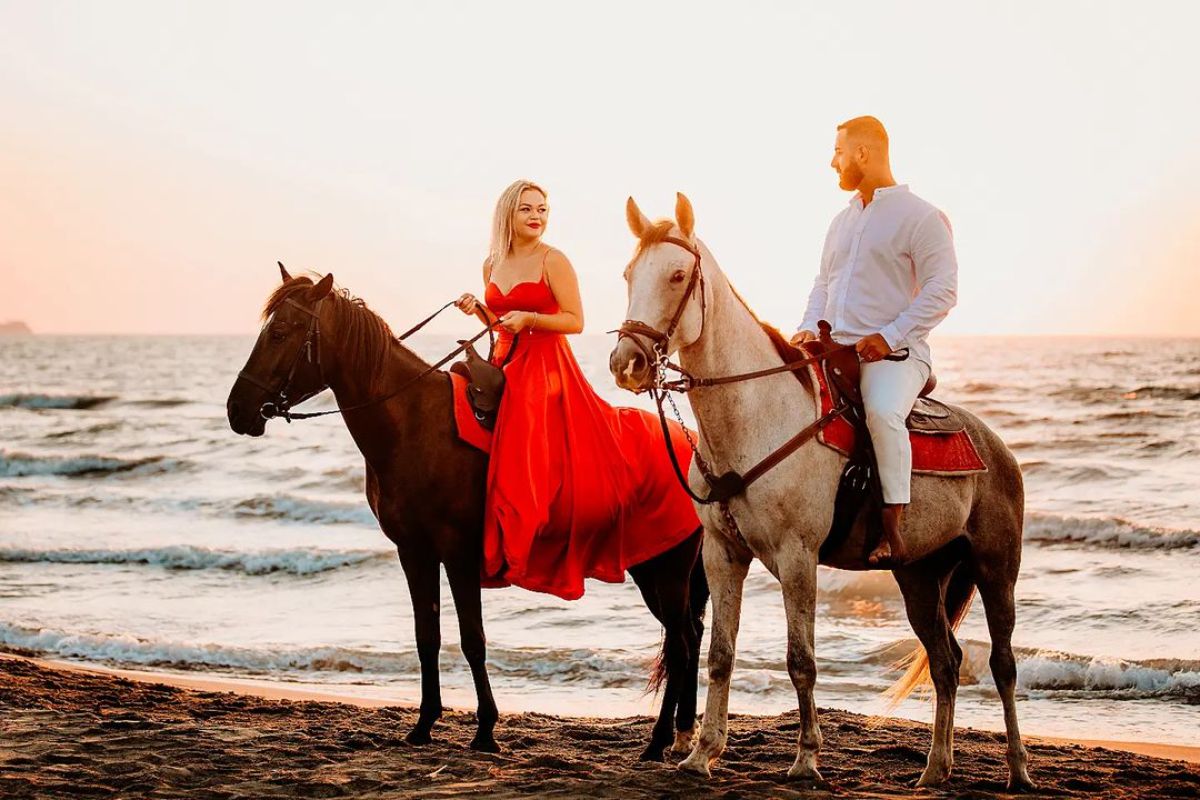 Man and woman enjoy a horse ride on the shore.