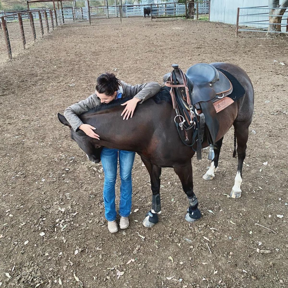 A woman pets a brown horse on a ranch.