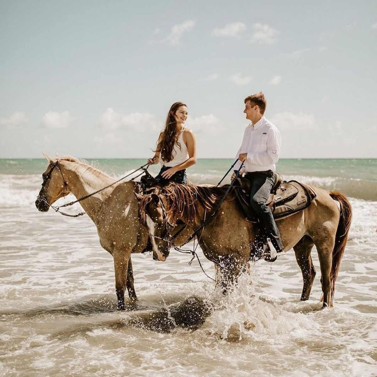 A young couple enjoys a horse ride on the shore.