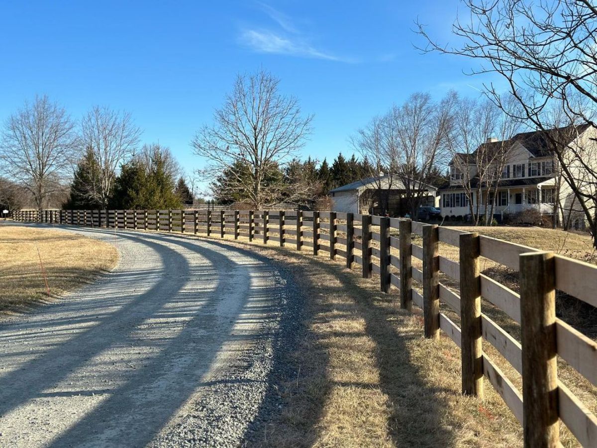 A wooden fence on a ranch near a road.