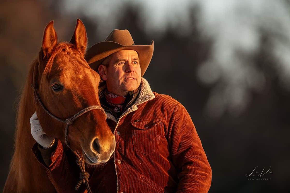 A man wears corduroy jacket pets a brown horse.