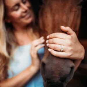 A woman with an engagement ring pets a brown horse.