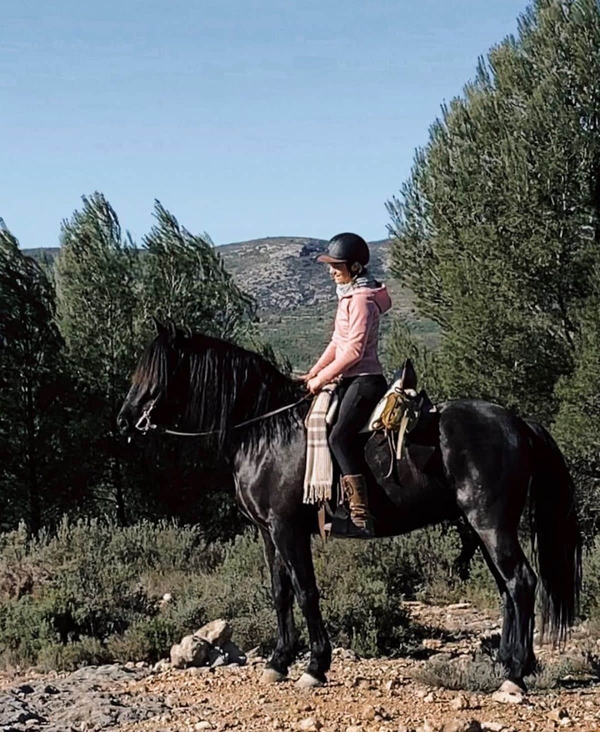 A young woman rides a black Andalusian horse.