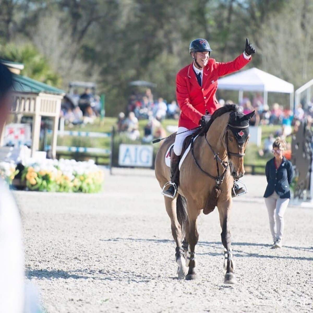 A male Equestrian rides with a red jacket rides a brown horse.