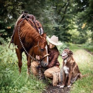 A cowboy, a dog, and a brown American Quarter Horse on a trail.